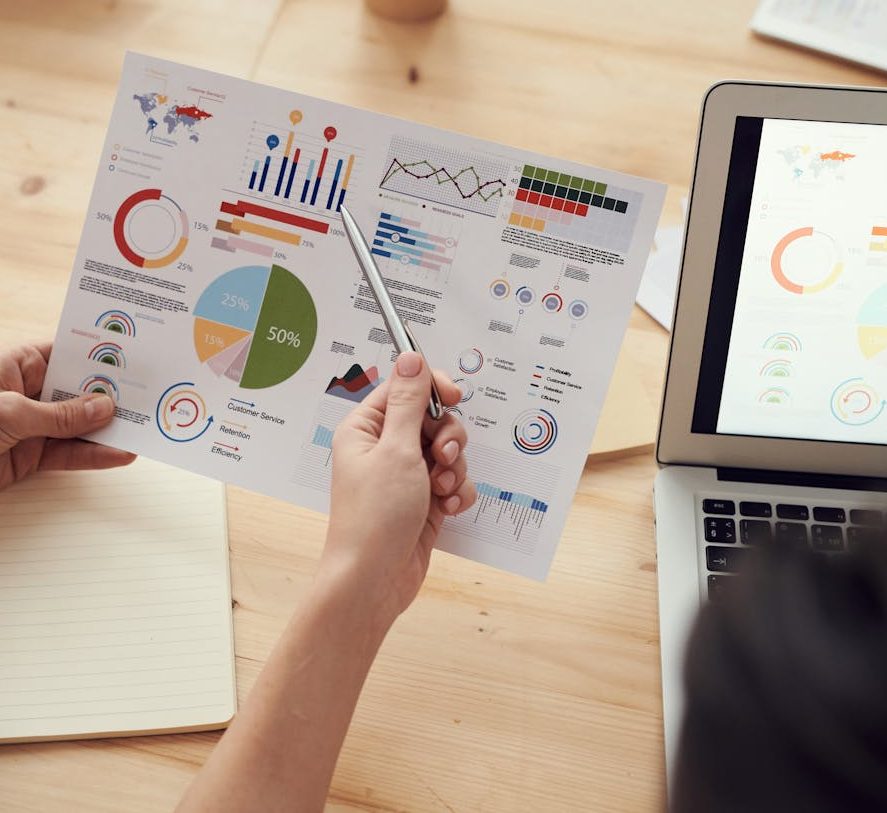 Hands pointing to a colorful chart with a laptop on the side